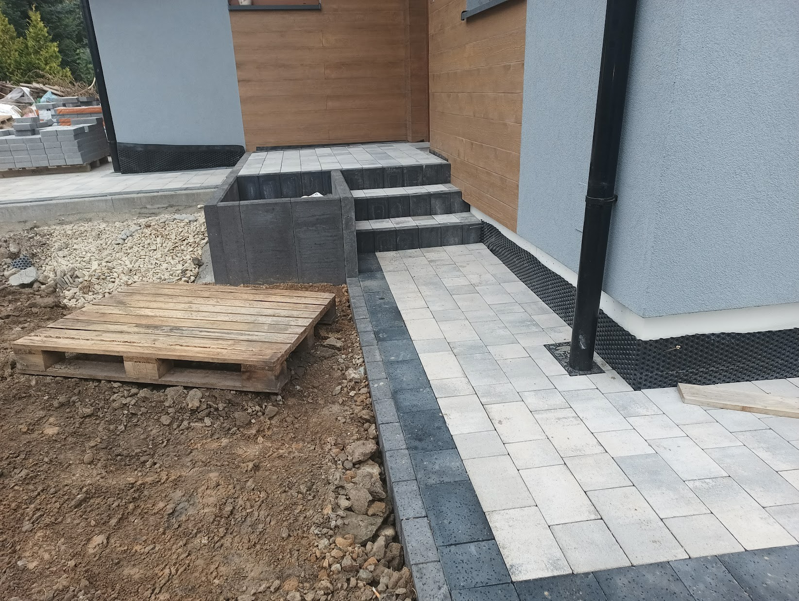 Ułożona kostka brukowa w Cieszynie tworząca ścieżkę i schody wejściowe do domu, widoczna paleta z kostką obok rozkopanej ziemi.