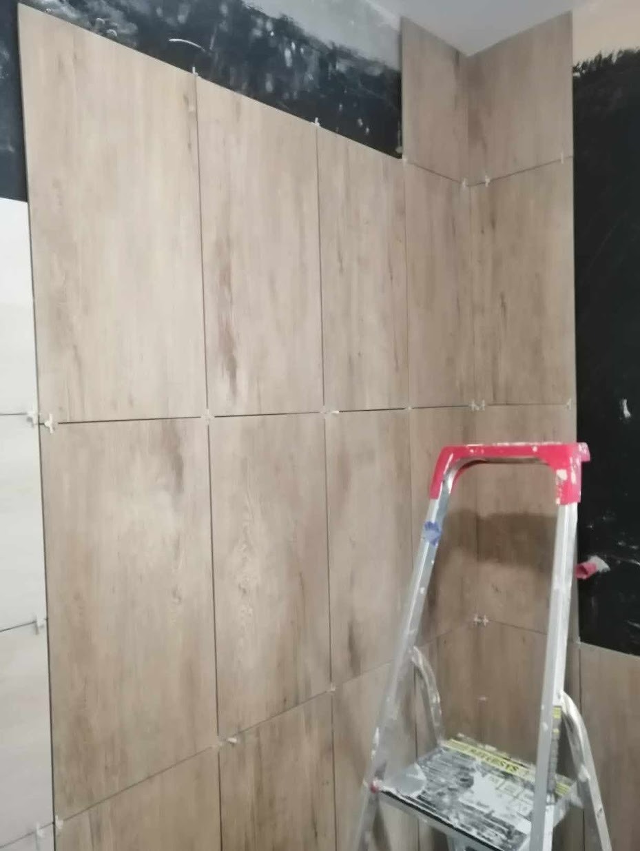 Ściana w trakcie wykańczania płytkami imitującymi drewno, widoczna drabina malarska i niezakończone prace na górze ściany.