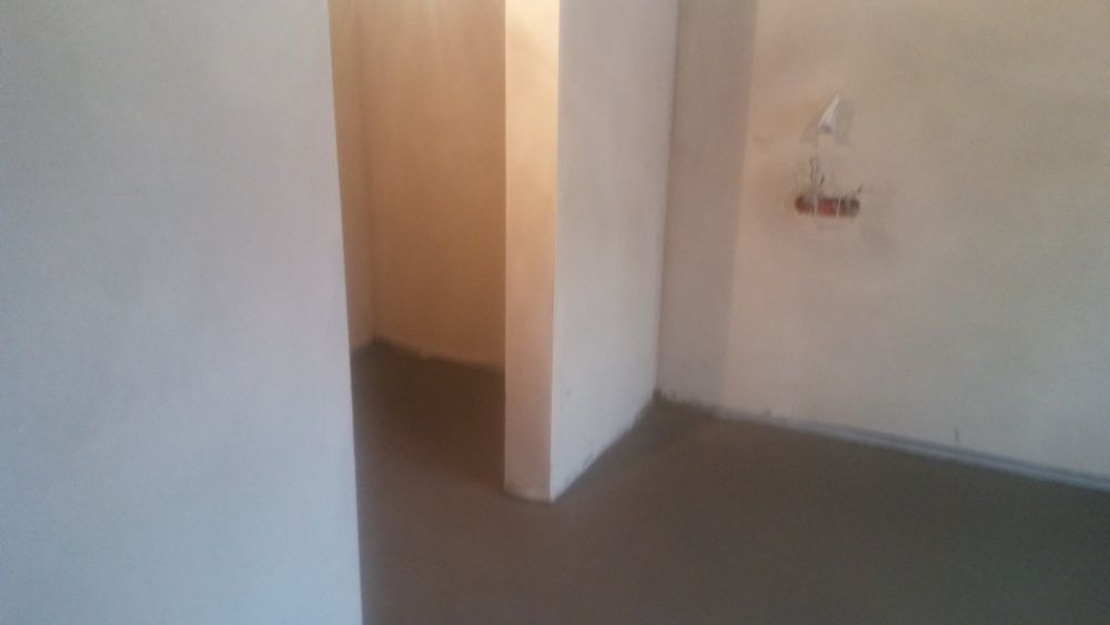 Wnętrze w trakcie prac wykończeniowych, świeżo położony, gładki, szary tynk na ścianach i podłodze, widoczne niedokończone gniazdko elektryczne.