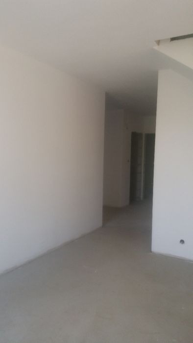 Surowe wnętrze pomieszczenia po nałożeniu tynków, widoczne ściany i podłoga w jasnych odcieniach szarości, przygotowane do dalszych prac wykończeniowych.