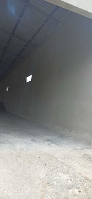 Wnętrze hali przemysłowej po nałożeniu tynków, widoczne dwa małe okna w górnej części ściany, surowy beton na podłodze.