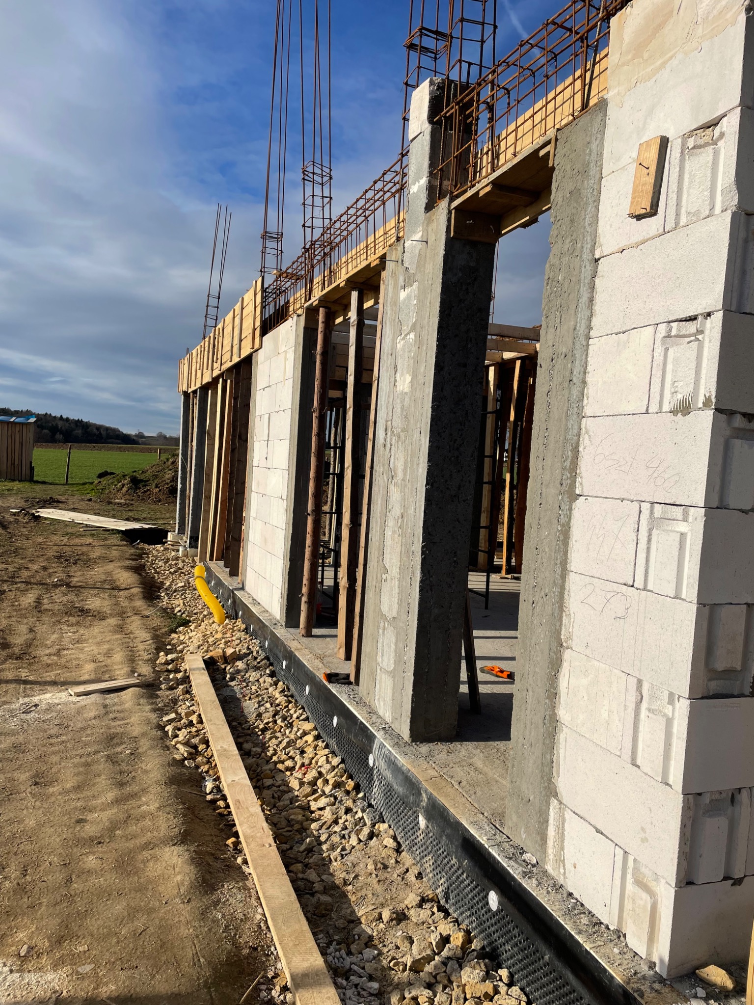 Wznoszenie ścian budynku z betonu komórkowego, widoczne zbrojenie i szalunki, w tle łąka i niebo.