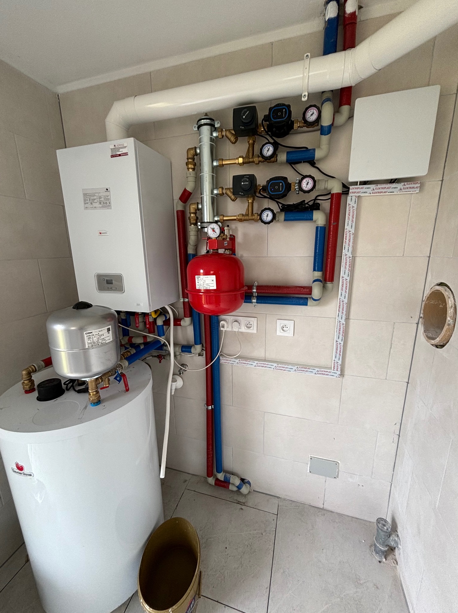 Nowoczesna kotłownia w jasnych płytkach, z piecem gazowym Saunier Duval, białym zasobnikiem wody, czerwonym naczyniem przeponowym CIMM, oraz kompletną instalacją hydrauliczną z pompami obiegowymi...