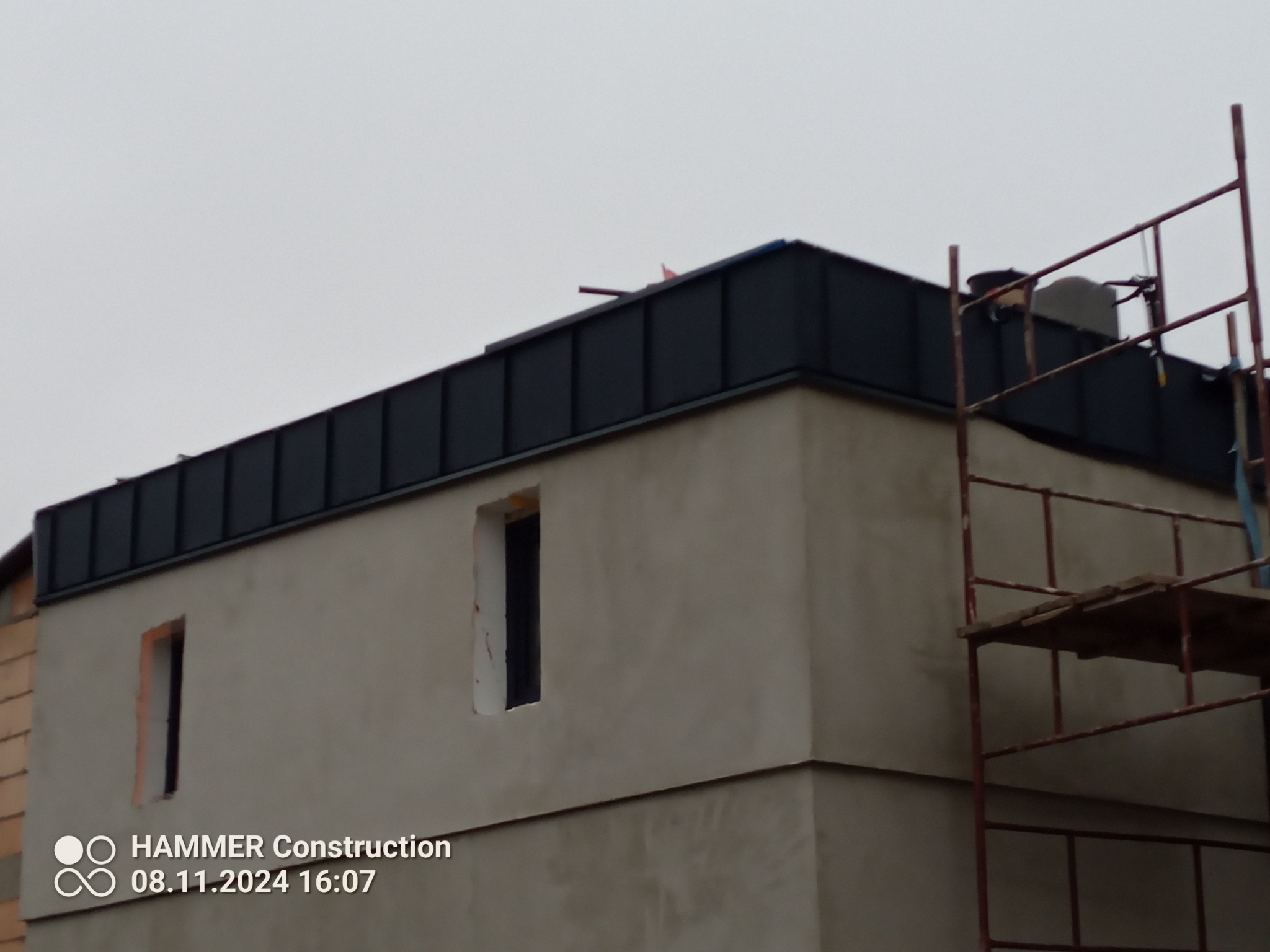 Nowe, ciemne poszycie dachu na budynku w trakcie budowy, widoczne rusztowanie i niezamaskowane otwory okienne.