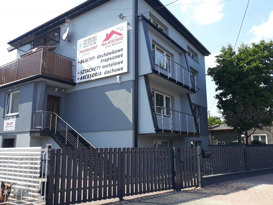 Budynek firmy Majerowie, producenta blach dachówkowych, trapezowych, szachet metalowych i akcesoriów dachowych, z biurem i sklepem na parterze, widoczny szyld reklamowy z numerami telefonów.
