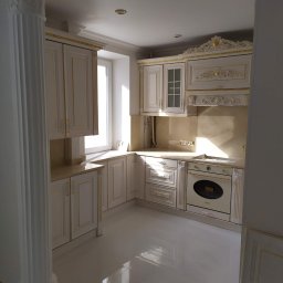 OLEKSII BIESIEDA - Elegancka, biała kuchnia z kolumną w stylu klasycystycznym, złotymi zdobieniami na meblach i błyszczącą podłogą.