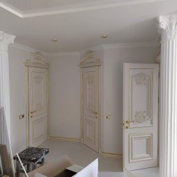 OLEKSII BIESIEDA - Wnętrze w trakcie prac wykończeniowych: białe, zdobione drzwi z pozłacanymi detalami, kolumny dekoracyjne z kapitelami, widoczny fragment sufitu podwieszanego i elementy robocze, kamera monitoringu...