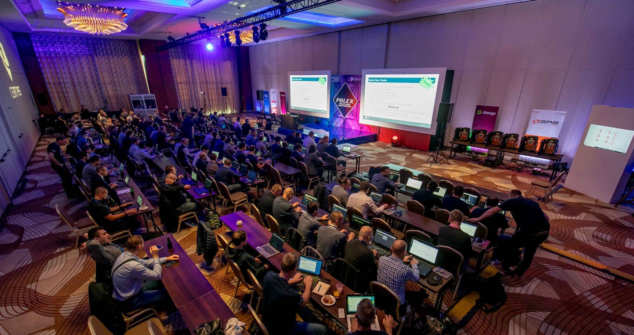 Sala konferencyjna wypełniona uczestnikami pracującymi na laptopach podczas prezentacji POLEX, z dwoma ekranami wyświetlającymi slajdy i logo Energa oraz GAZ po prawej stronie sceny.