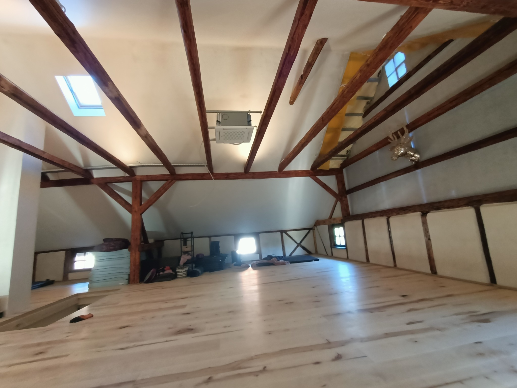 Klimatyzacja sufitowa zamontowana w przestrzeni poddasza z widocznymi drewnianymi belkami stropowymi i oknami dachowymi.