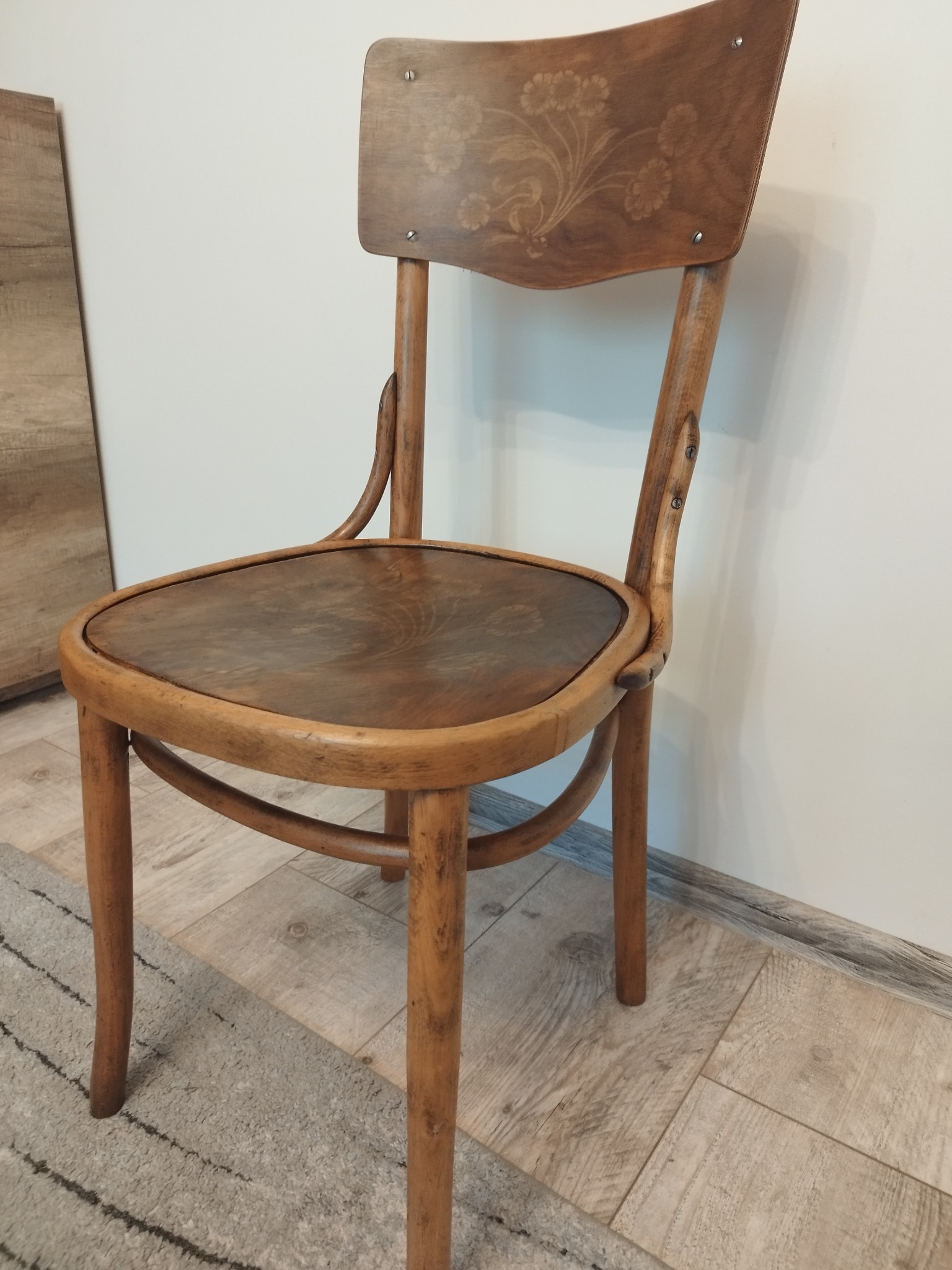 Drewniane krzesło z giętymi elementami, ozdobione motywem kwiatowym na oparciu, widoczne ślady użytkowania i patyna.