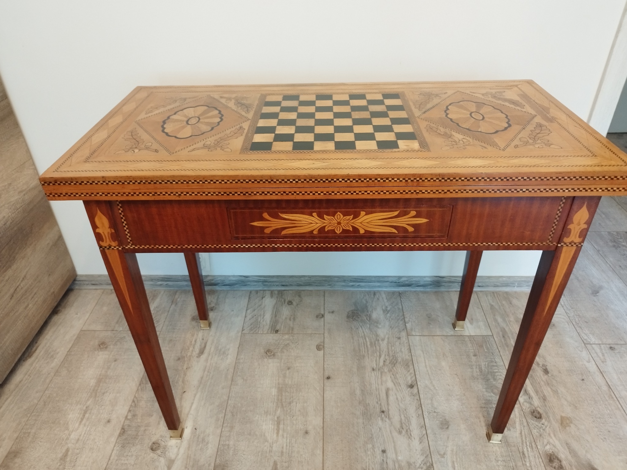 Masywny, drewniany stół do gry w szachy z szufladą i intarsjami kwiatowymi, wykończony na wysoki połysk, z metalowymi nakładkami na nogach.