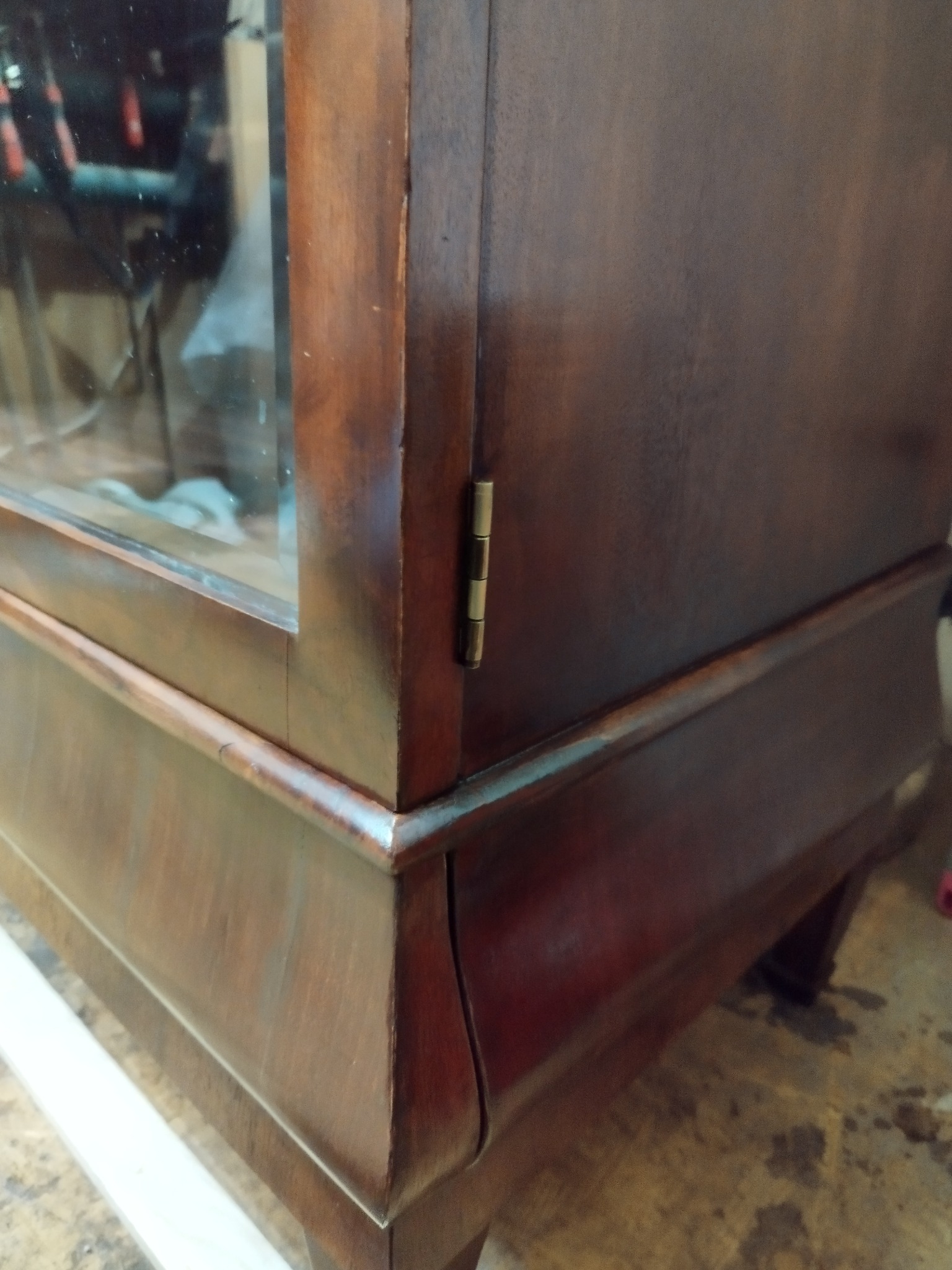 Fragment odnowionej, brązowej witryny z przeszklonym frontem, ukazujący zawias drzwi i detale wykończenia.