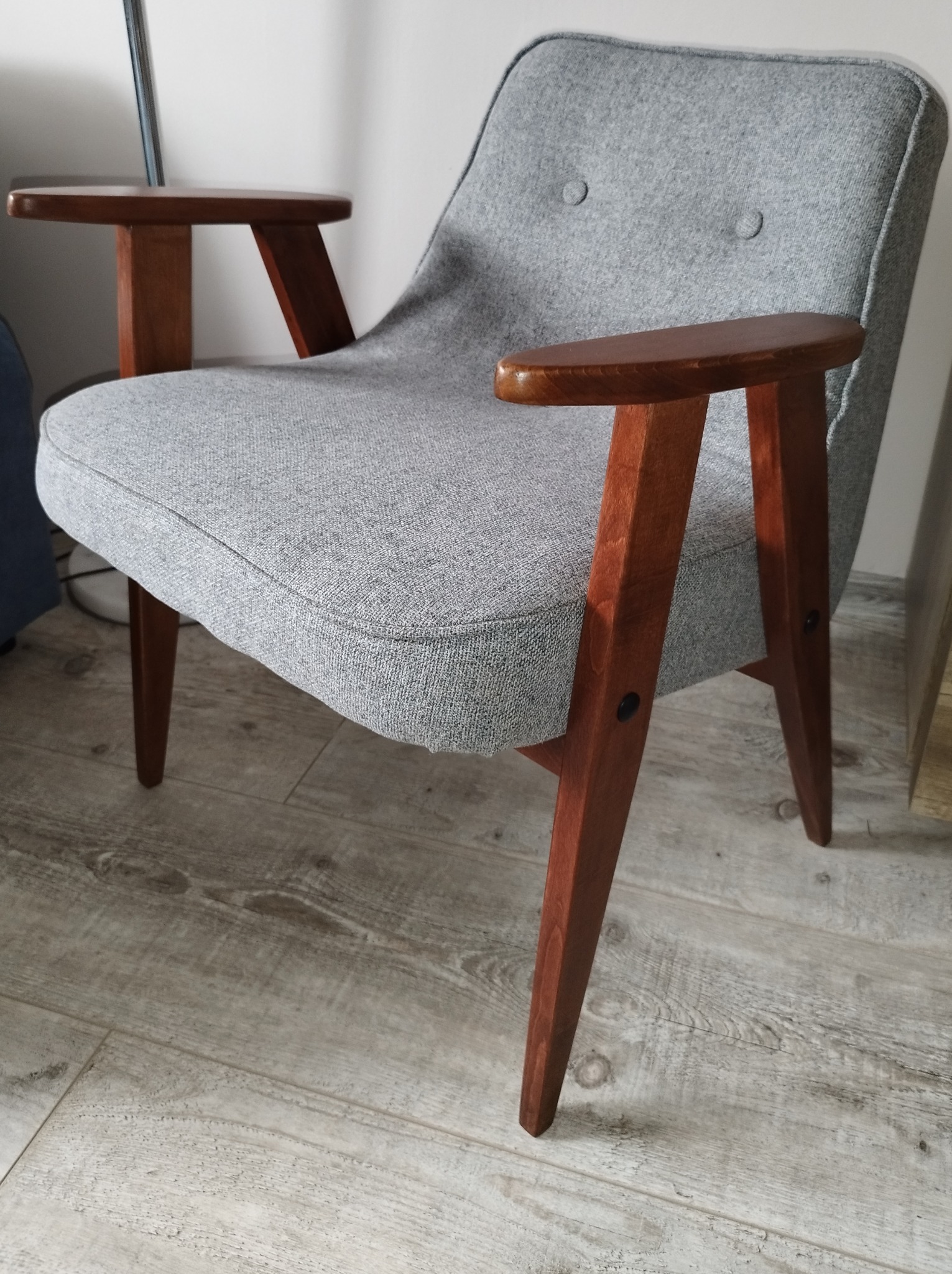 Odrestaurowany fotel w stylu retro z szarą tapicerką i drewnianymi podłokietnikami, widoczne detale łączeń nóg.