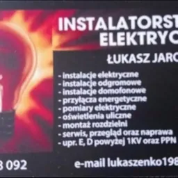 Wizytówka firmy instalatorstwa elektrycznego Łukasza Jarońskiego z grafiką żarówki na czerwonym tle, zawierająca dane kontaktowe i listę oferowanych usług.