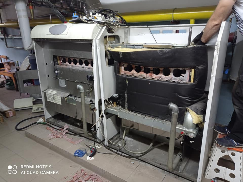 Demontaż i inspekcja wnętrza pieca CO z widocznymi rurami, palnikiem i izolacją termiczną, podczas prac serwisowych hydraulika w pomieszczeniu kotłowni.