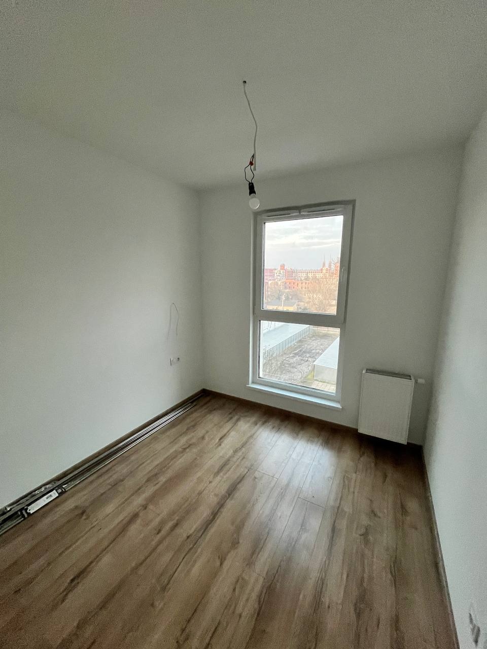 Pokój po ułożeniu paneli podłogowych w Warszawie, widoczne listwy przypodłogowe i surowa żarówka.