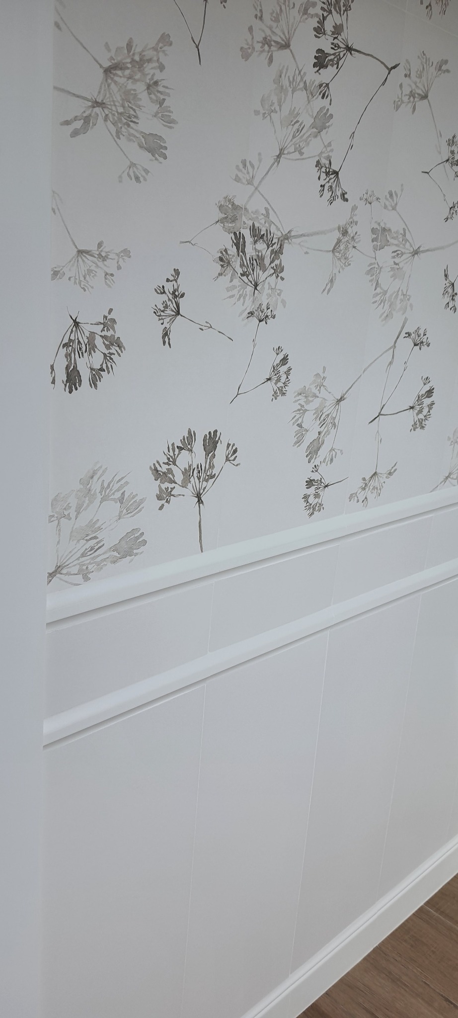 Ściana z panelami dekoracyjnymi w dolnej części i tapetą w delikatny, kwiatowy wzór w górnej części.