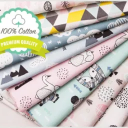 Stos bawełnianych tkanin z dziecięcymi wzorami: geometryczne figury, góry, chmury, łabędzie, lisy i jeże, z naklejką '100% Cotton Premium Quality'.