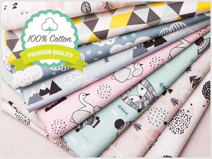 Stos bawełnianych tkanin z dziecięcymi wzorami: geometryczne figury, góry, chmury, łabędzie, lisy i jeże, z naklejką '100% Cotton Premium Quality'.