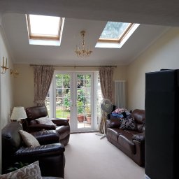 Olnada - Jasne wnętrze salonu z dwoma oknami dachowymi, skórzanymi meblami wypoczynkowymi i widokiem na ogród przez przeszklone drzwi balkonowe.