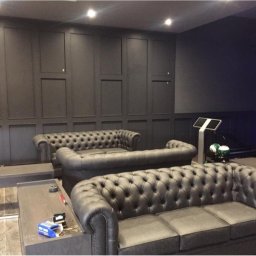 Olnada - Eleganckie wnętrze w odcieniach szarości z panelami ściennymi, skórzanymi sofami Chesterfield i elementami wyposażenia siłowni.