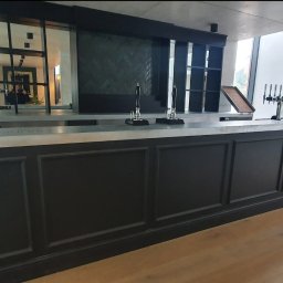 Olnada - Wykończony bar z ciemnymi panelami i marmurowym blatem, widoczne krany do piwa i elementy wystroju wnętrza w tle.