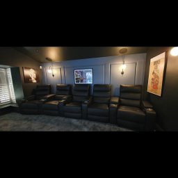 Olnada - Kino domowe z pięcioma czarnymi, skórzanymi fotelami z uchwytami na napoje, podświetlonymi kinkietami i dekoracjami ściennymi, w tym plakatem Bruce Lee.