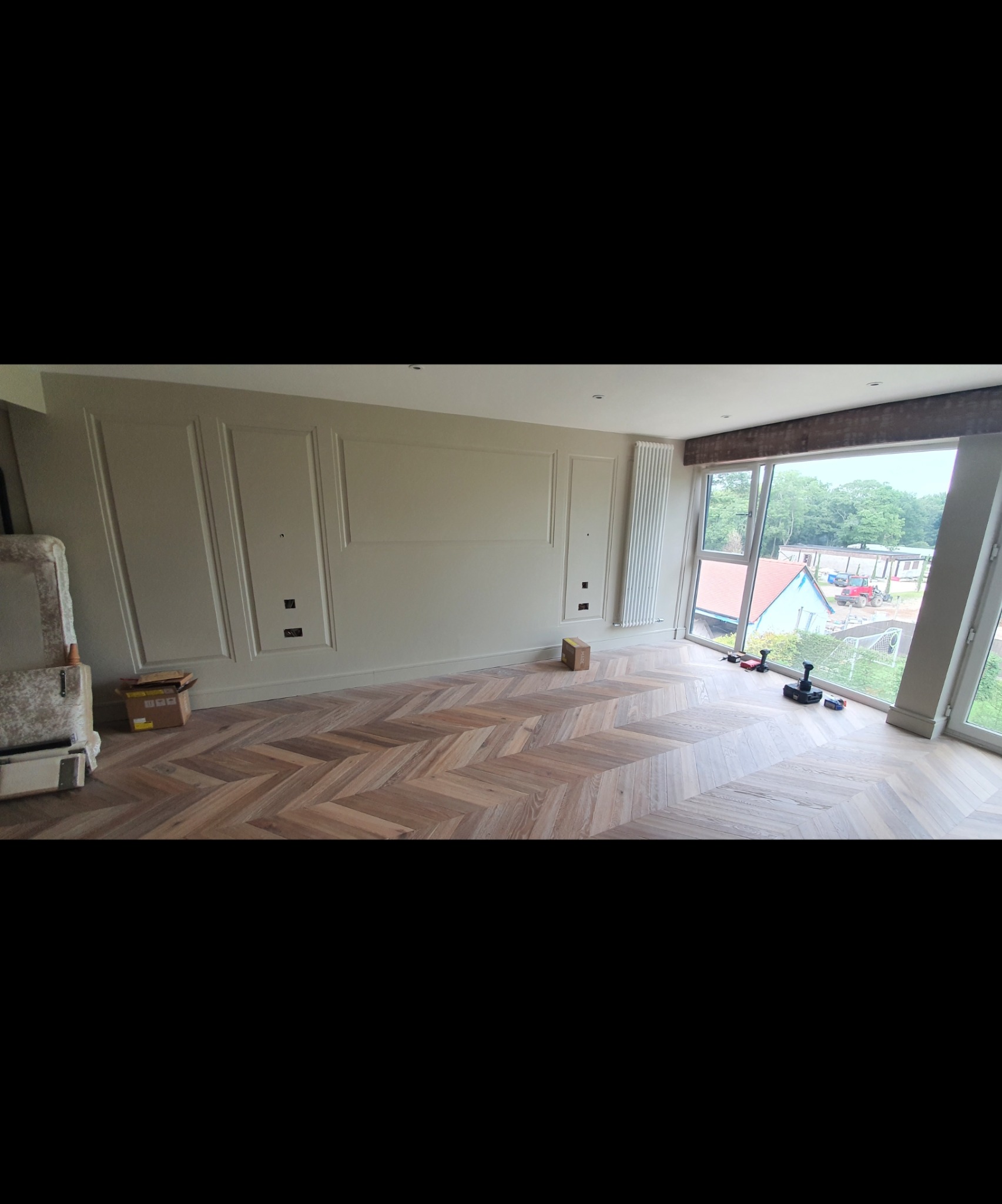 Salon z nowo ułożonym parkietem w jodełkę, ściany w odcieniach beżu z dekoracyjnymi panelami, widoczne narzędzia i kartonowe pudełka po materiałach.