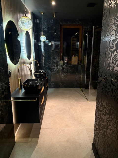 Elegancka łazienka z czarnymi marmurowymi ścianami, podwójną umywalką na szafce i okrągłymi lustrami z podświetleniem LED. Nowoczesny design z akcentami złota.
