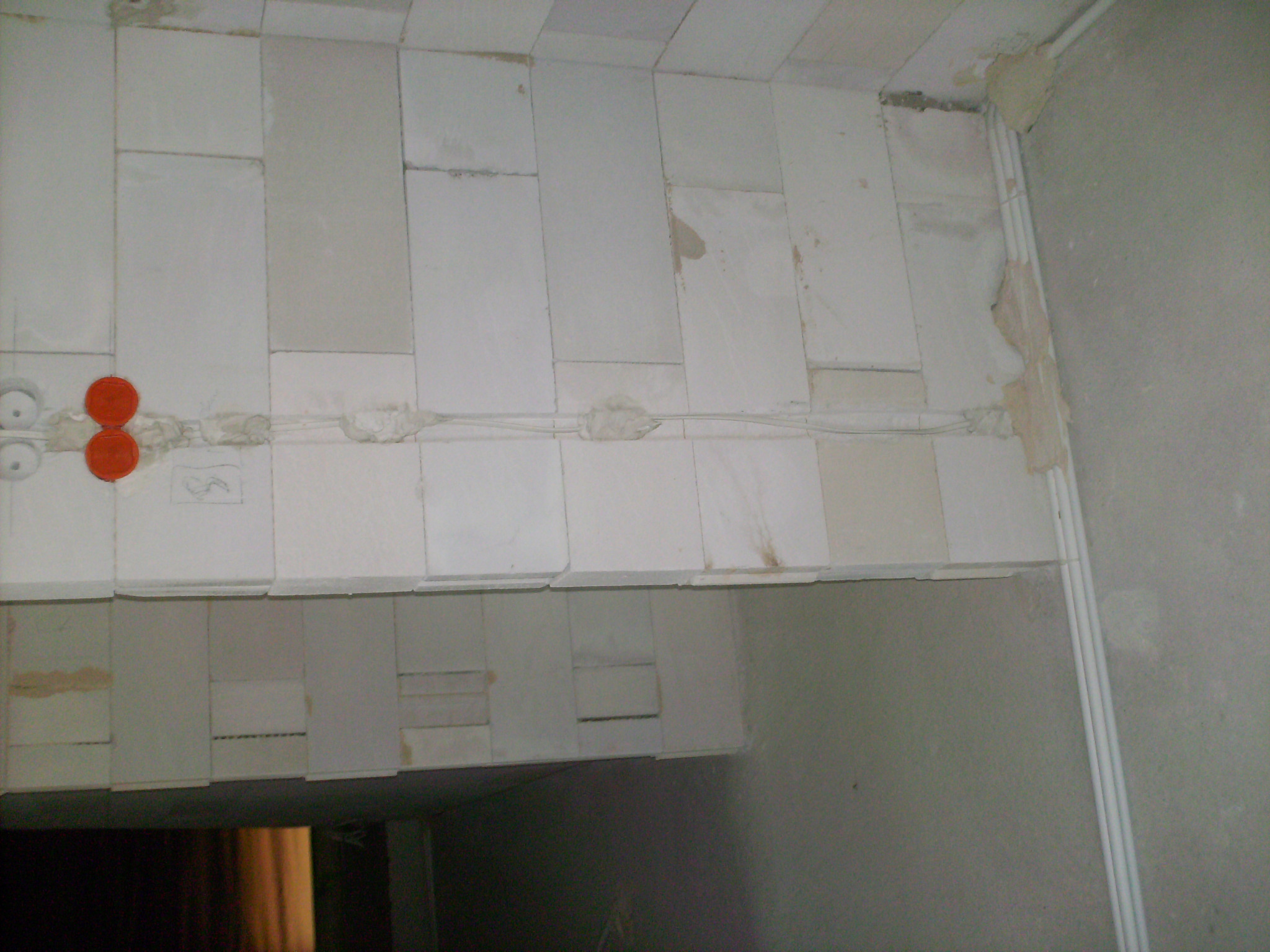 Niedokończona instalacja elektryczna w ścianie z białych bloczków, widoczne kable zabezpieczone taśmą i puszki elektryczne z czerwonymi pokrywkami.