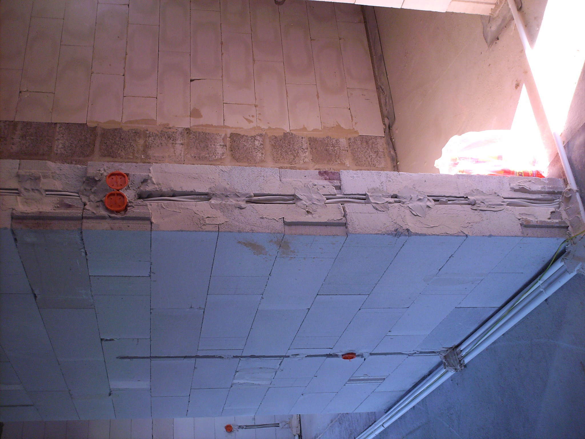 Instalacja elektryczna w trakcie montażu w ścianie z pustaków, widoczne przewody w bruzdach i puszki elektryczne, częściowo zamurowane.