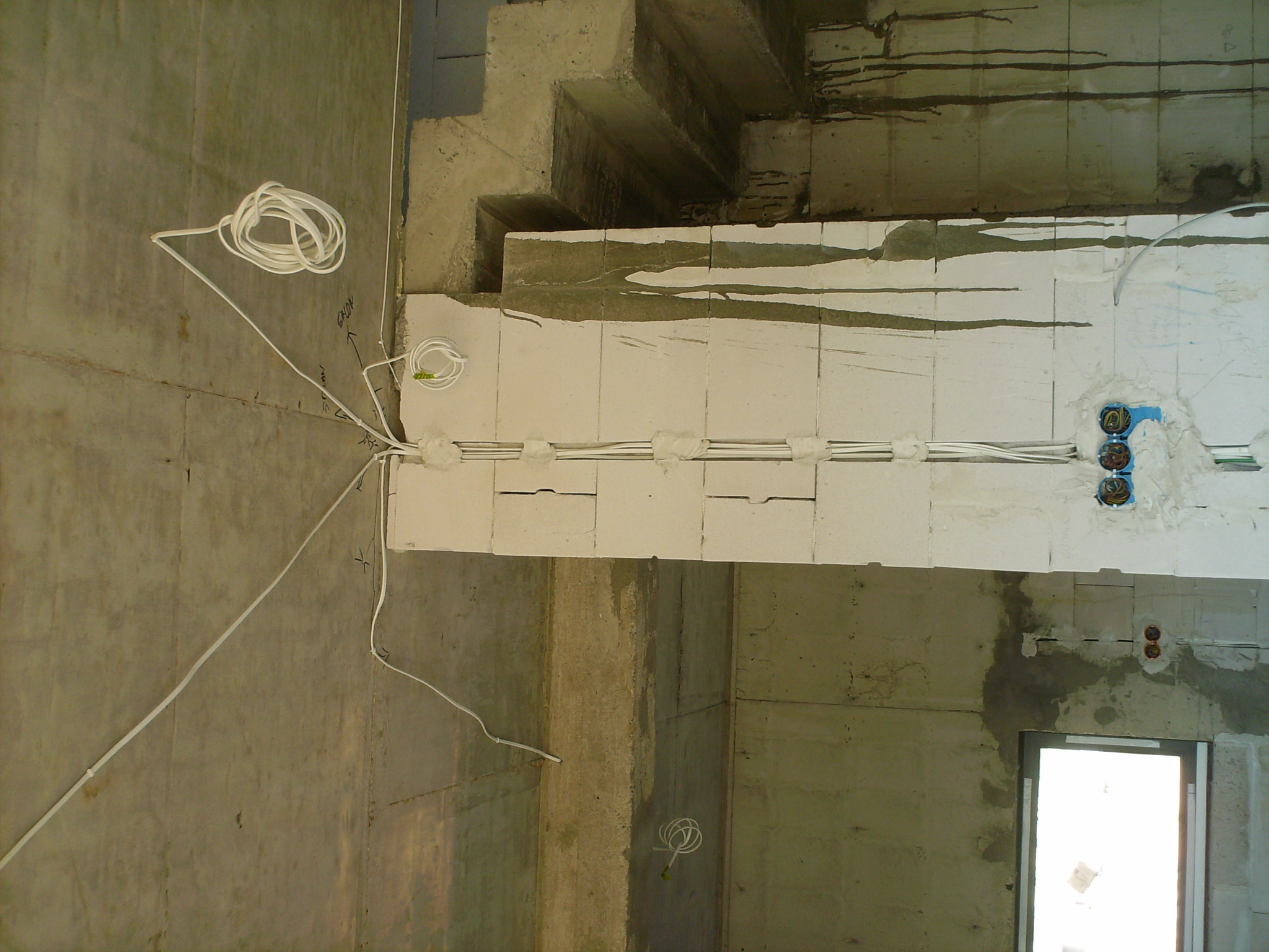 Surowy stan budynku: kable elektryczne prowadzone w ścianach z betonu komórkowego, widoczne puszki instalacyjne i zwój kabli na ścianie, przygotowanie do tynkowania.