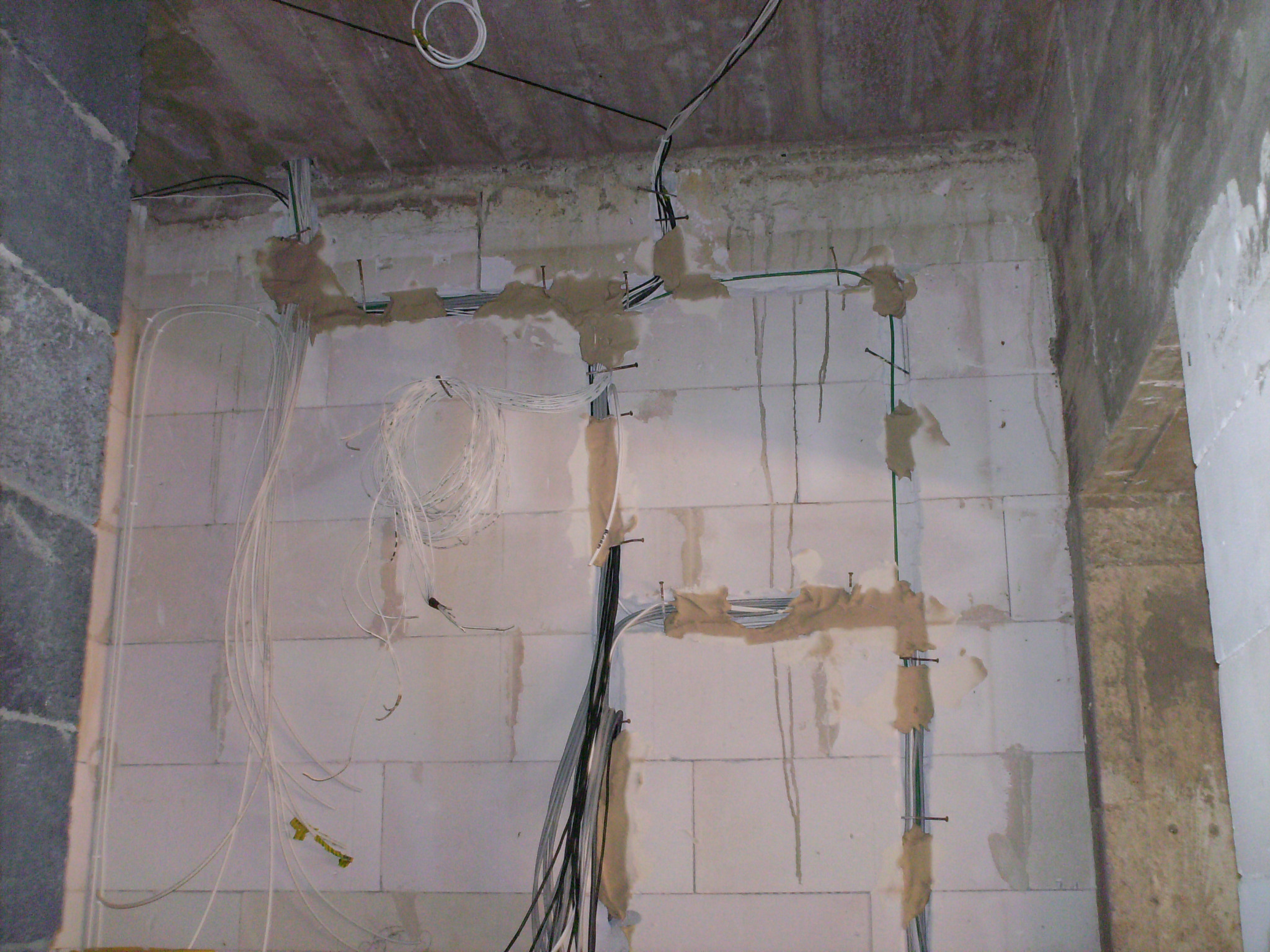 Surowy stan: Instalacja przewodów elektrycznych w nowym budynku z pustaków, kable mocowane do ściany za pomocą gwoździ i zaprawy.