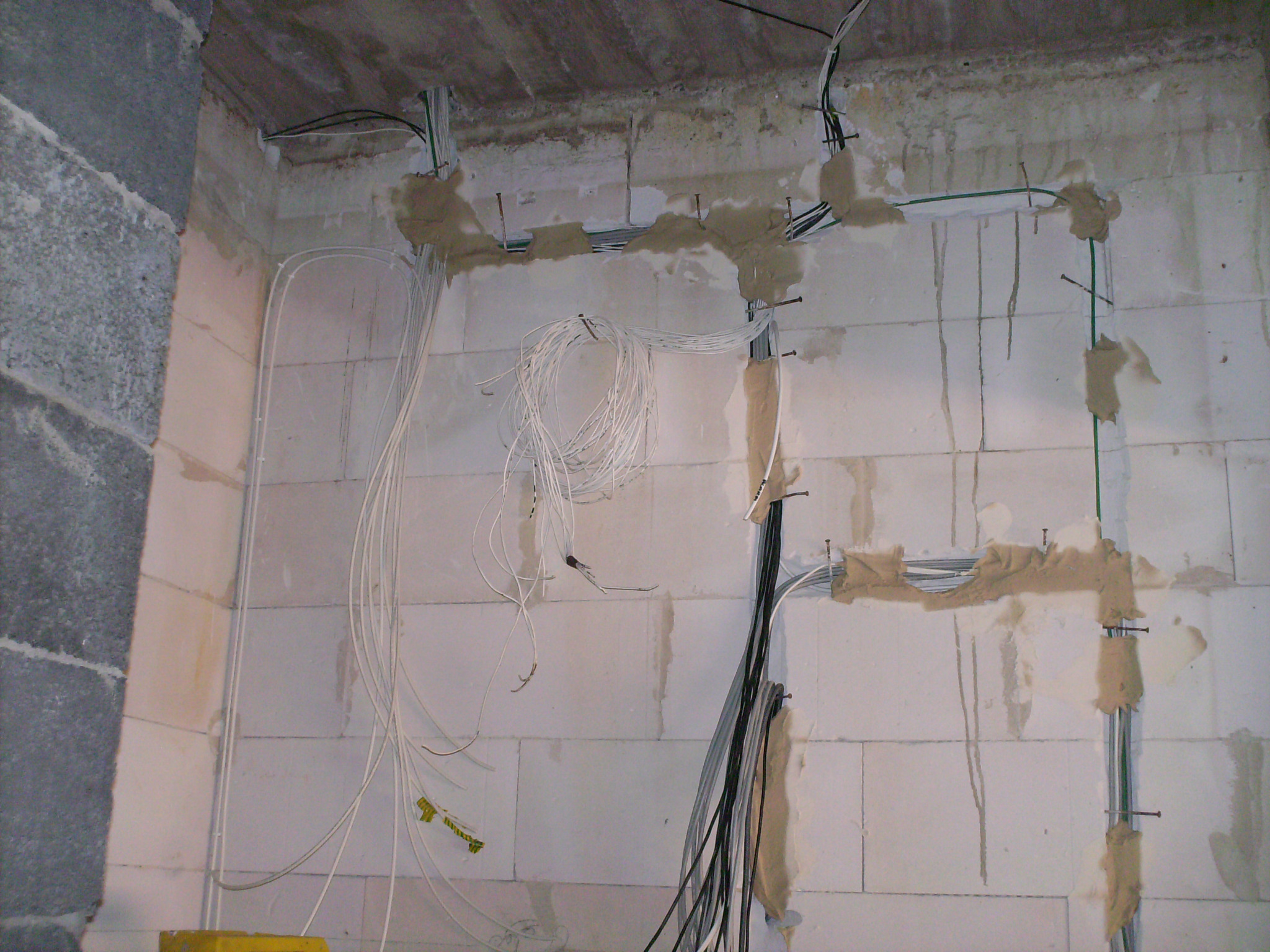 Ściana z betonu komórkowego w trakcie montażu przewodów elektrycznych, kable przytwierdzone gwoździami i częściowo zamaskowane zaprawą.