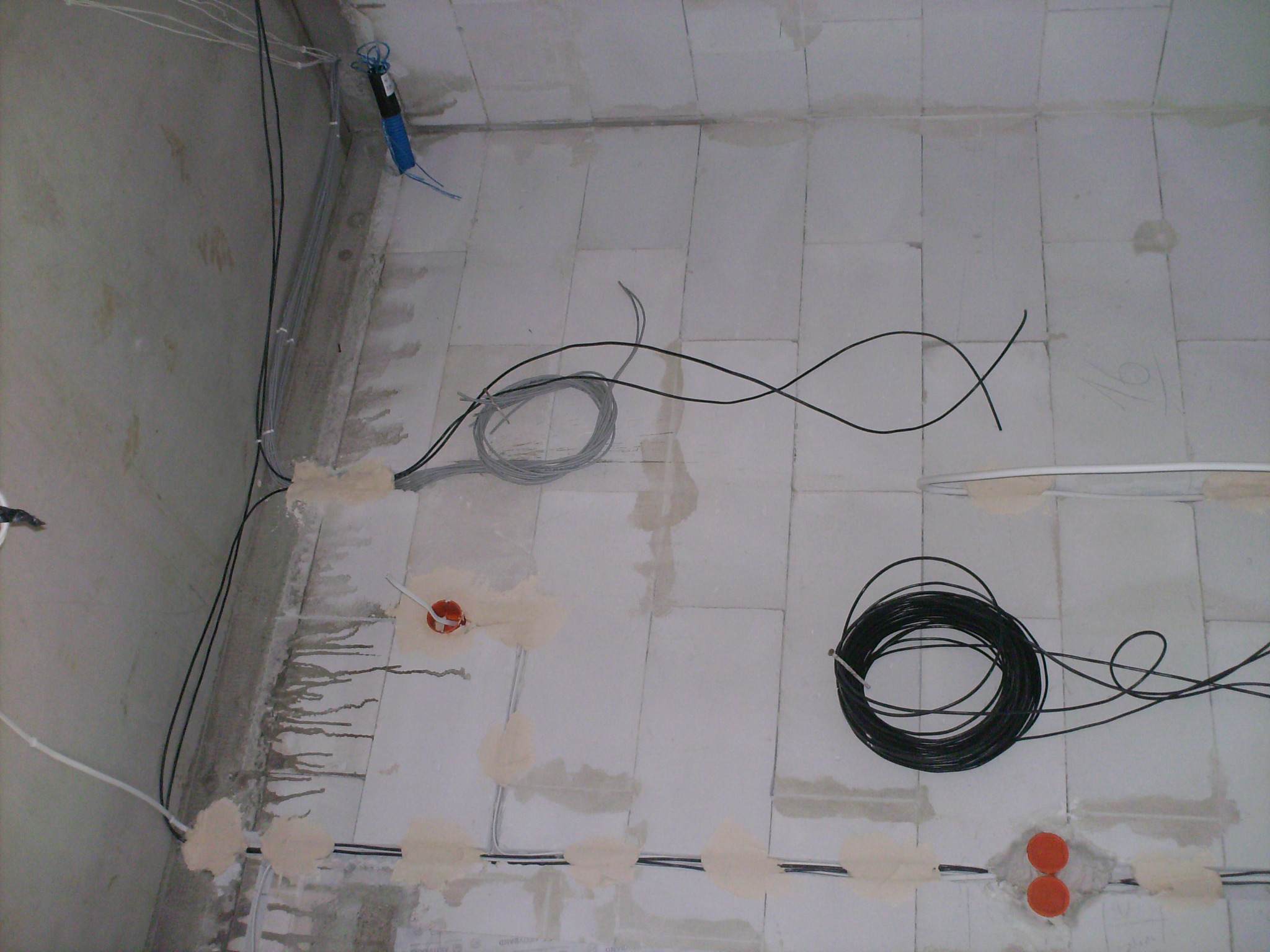 Surowy stan instalacji elektrycznej w nowym budownictwie: przewody rozprowadzone po ścianach z betonu komórkowego, puszki instalacyjne zamontowane, niektóre przewody zwinięte w kłębek.