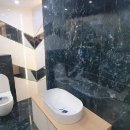 Nowoczesna łazienka z umywalką nablatową na szafce z drewnopodobnym blatem, ciemne marmurowe płytki na ścianie i podłodze, oraz lustrzane elementy dekoracyjne.