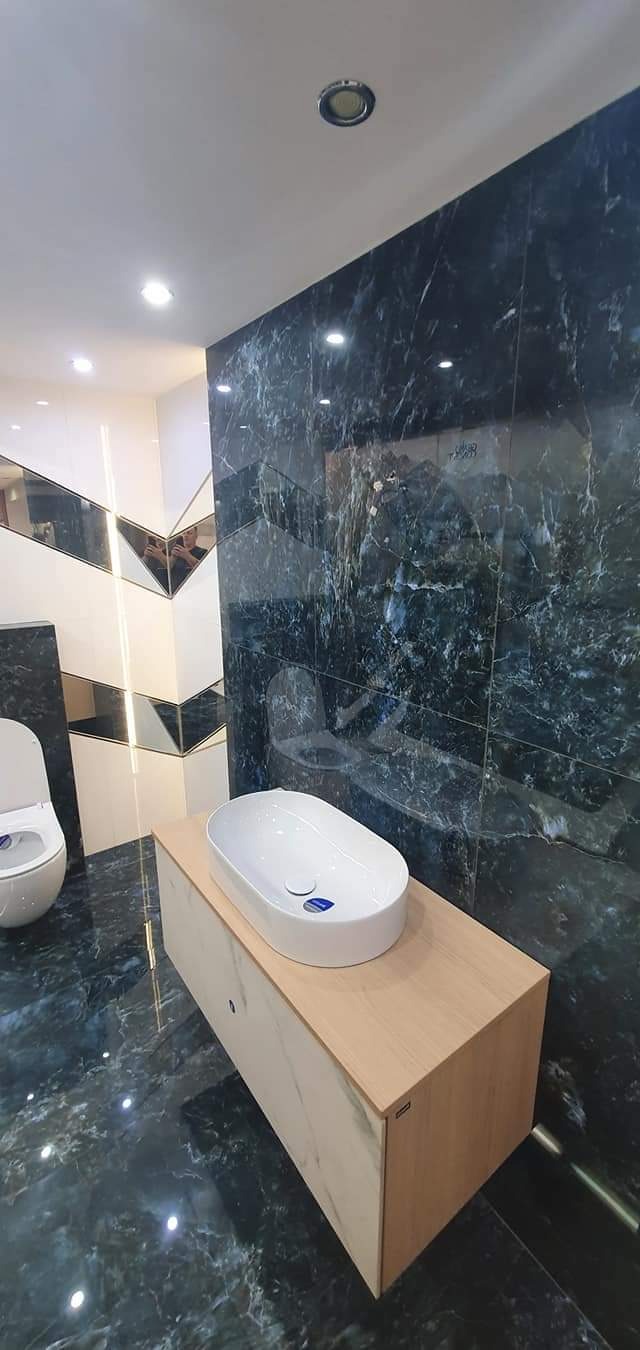 Nowoczesna łazienka z umywalką nablatową na szafce z drewnopodobnym blatem, ciemne marmurowe płytki na ścianie i podłodze, oraz lustrzane elementy dekoracyjne.