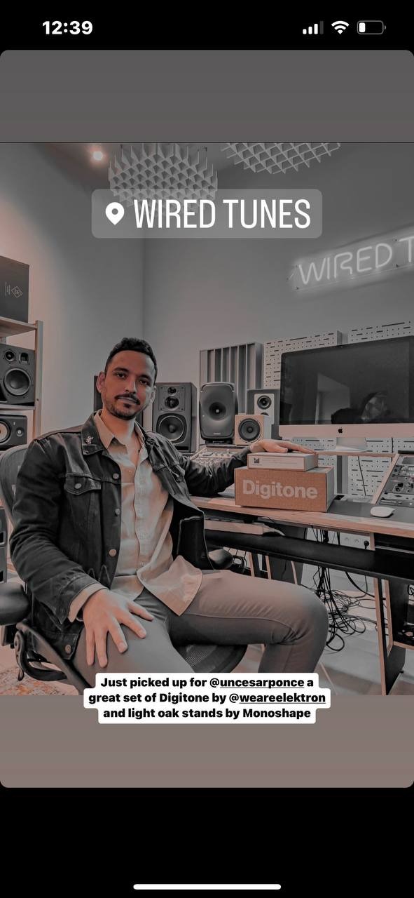 Mężczyzna siedzi w studiu nagraniowym, otoczony monitorami studyjnymi, panele akustyczne na suficie, neonowy napis 'Wired Tunes' w tle.