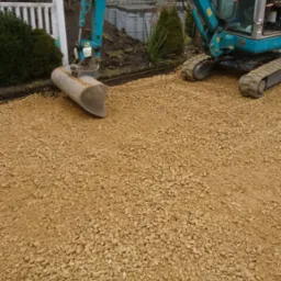 Niebieska mini koparka Sunward na podsypce żwirowej, przygotowanie terenu pod kostkę brukową, widoczna granica wykopu wyznaczona sznurkiem.