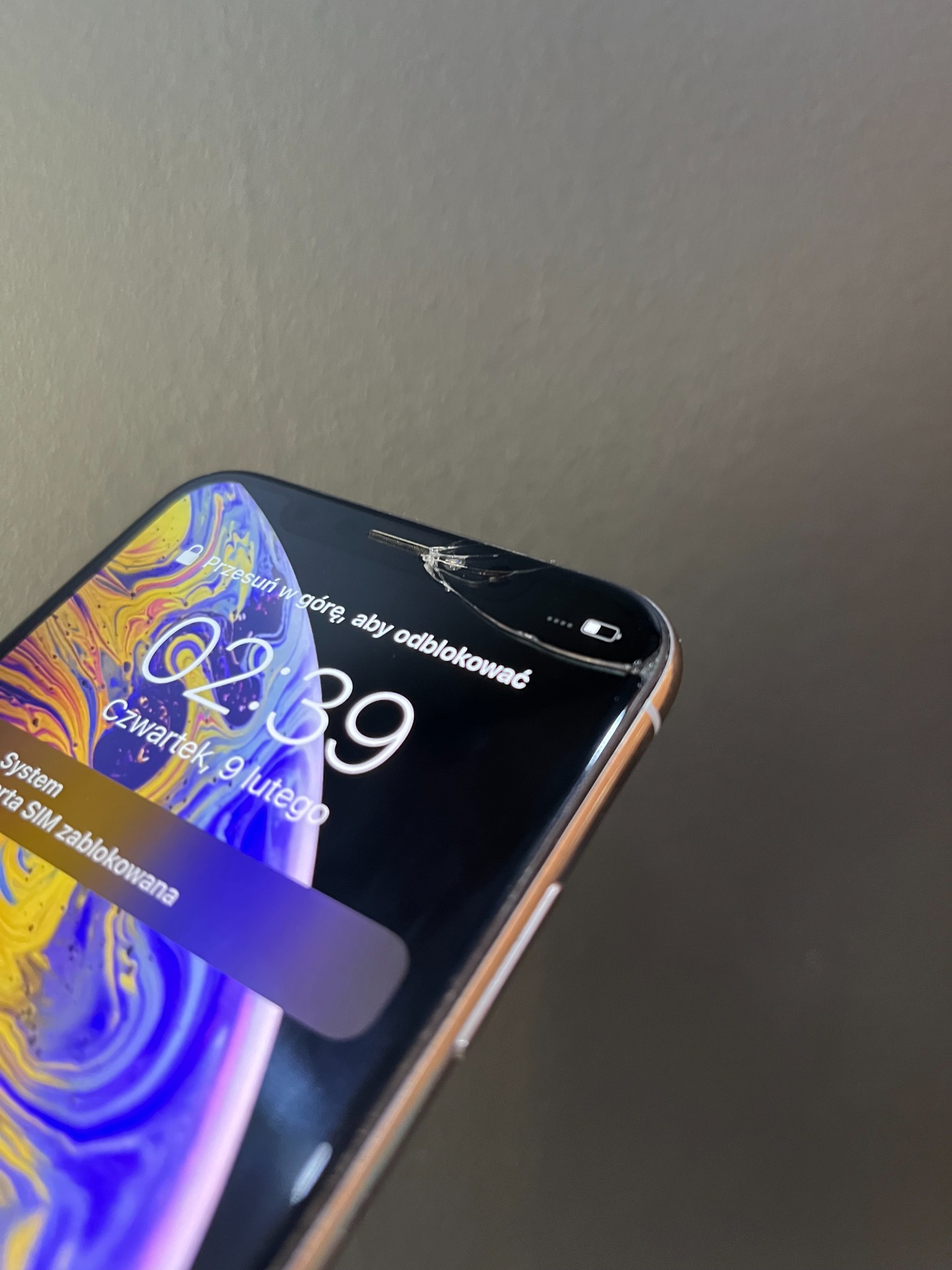 Smartfon z pękniętym ekranem w prawym górnym rogu, wyświetlający godzinę 02:39 i datę 9 lutego, z komunikatem o zablokowanej karcie SIM.