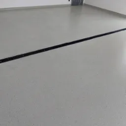 Jasnoszara, błyszcząca posadzka z drobnymi, ciemnymi inkluzjami w nowym pomieszczeniu, z widocznym liniowym odpływem podłogowym.