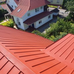 MW Team - Czerwony dach z blachy falistej na tle białego domu z czerwonym dachem, widok z góry, słoneczny dzień.