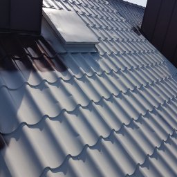 MW Team - Częściowo pomalowany na biało dach z blachy trapezowej, widoczny komin i okno dachowe, kontrastujące fragmenty w oryginalnym brązowym kolorze.