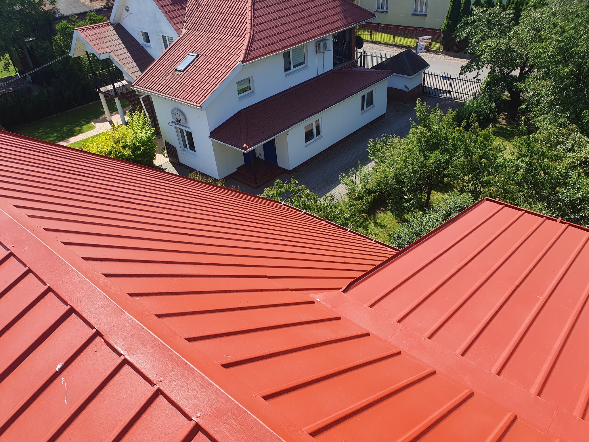 Czerwony dach z blachy falistej na tle białego domu z czerwonym dachem, widok z góry, słoneczny dzień.