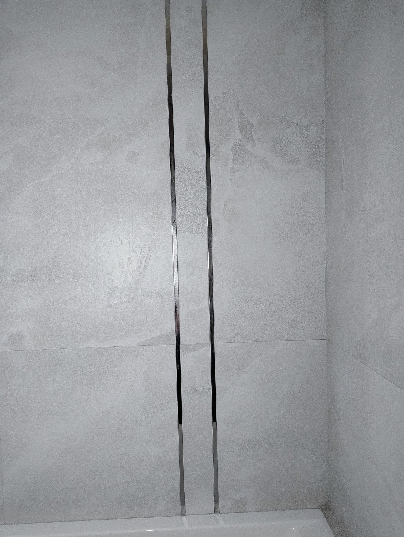 Jasnoszare płytki imitujące marmur z metalowymi listwami dekoracyjnymi w pionie, wykończenie ściany w łazience, widok z dołu.