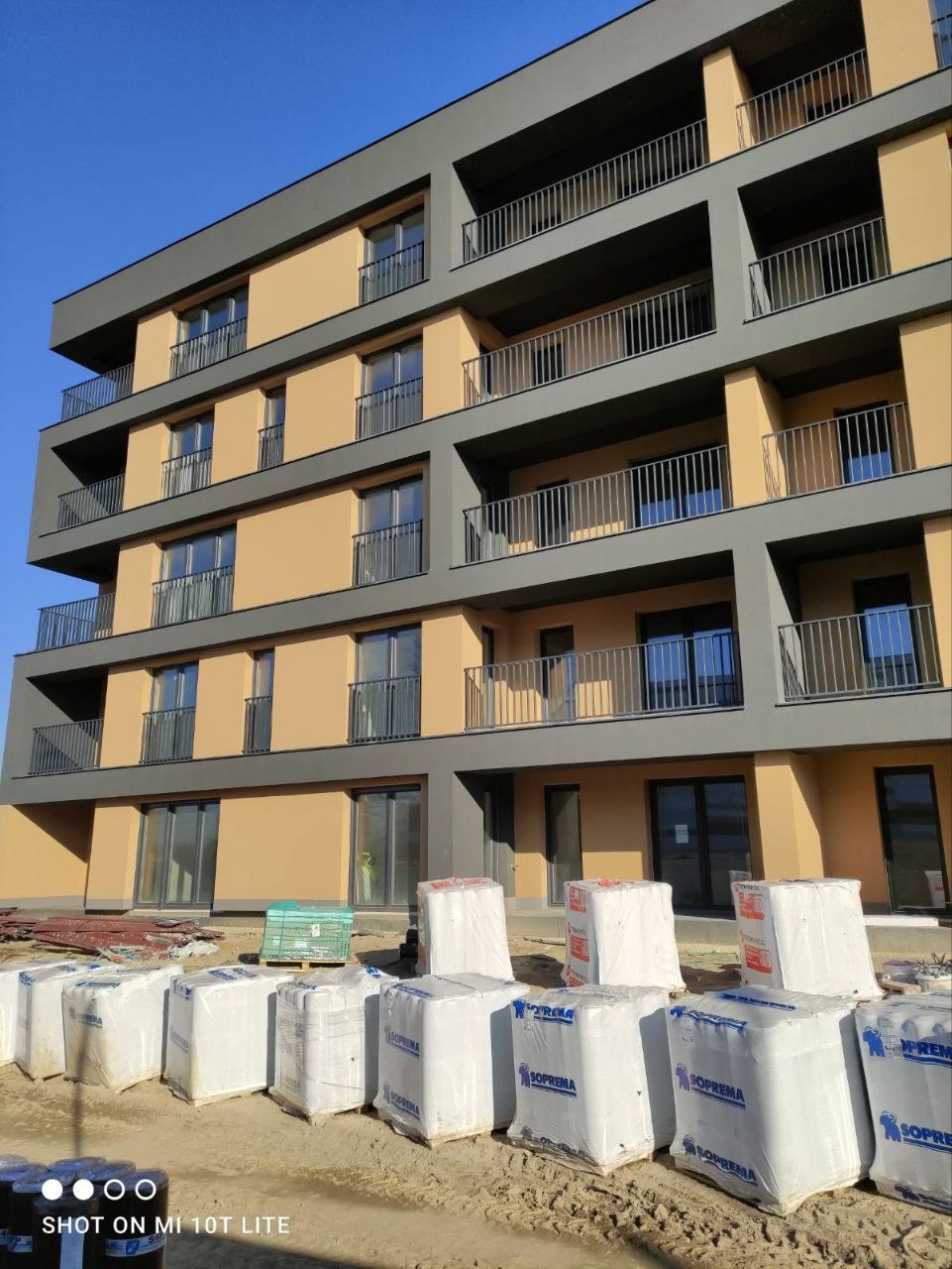 Nowoczesny blok mieszkalny w trakcie ocieplania elewacji, widoczne opakowania wełny mineralnej SOPREMA na pierwszym planie.