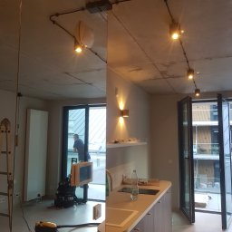 HUBERT - Złota Rączka - - Nowoczesne wnętrze z surowym betonowym sufitem i widocznymi instalacjami elektrycznymi, z reflektorami szynowymi i kinkietami, odzwierciedlone w dużym lustrze, z widocznym wyposażeniem...