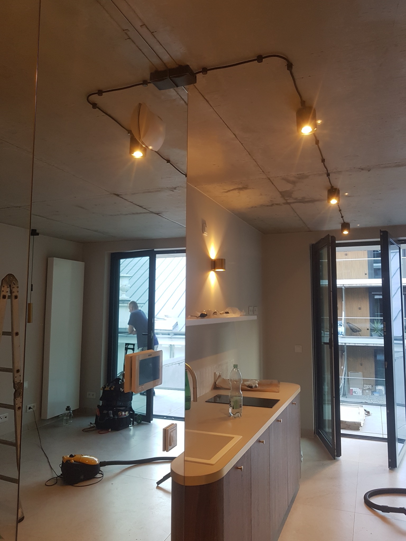 Nowoczesne wnętrze z surowym betonowym sufitem i widocznymi instalacjami elektrycznymi, z reflektorami szynowymi i kinkietami, odzwierciedlone w dużym lustrze, z widocznym wyposażeniem...