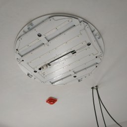 Fotovolt - Widok od dołu na okrągłą lampę LED w trakcie montażu na białym suficie, widoczne przewody elektryczne i czujnik dymu.