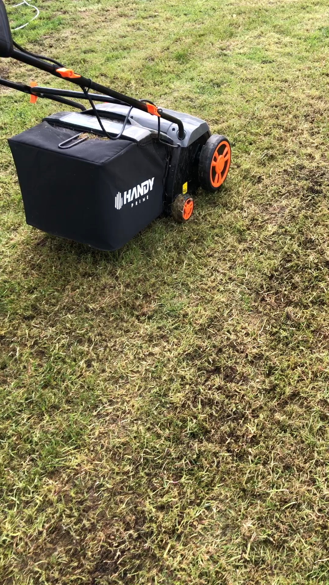 Aerator Handy Prime na trawniku z widocznymi śladami po aeracji, zbierający mech i filc.